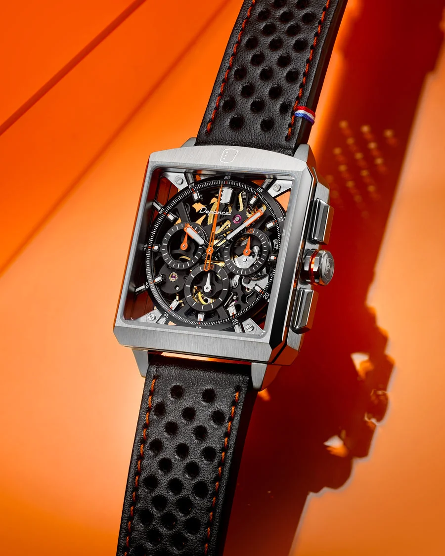 Luxury square silver Depancel skeleton watch with black perforated strap, orange accents, on orange background.