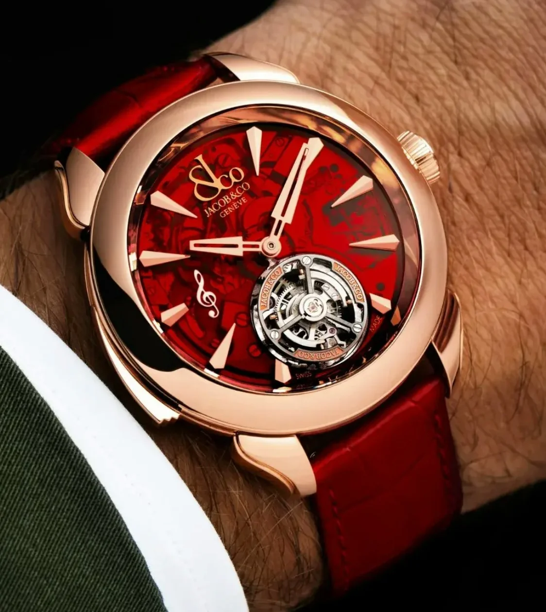Jacob & Co. rose gold watch with a red dial, flying tourbillon, & treble clef on a red strap, worn on a wrist.