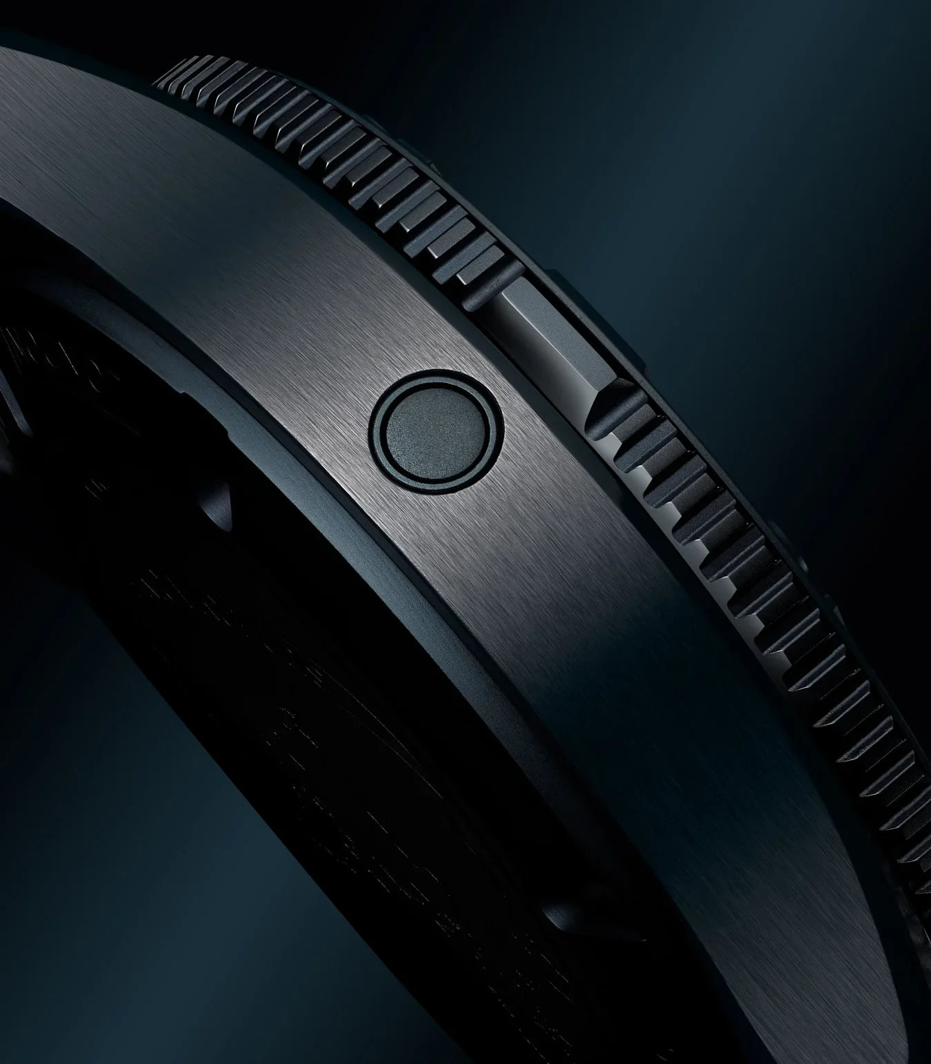 Close-up of a dark, brushed luxury watch case with a round pusher and a deeply ridged rotating bezel.