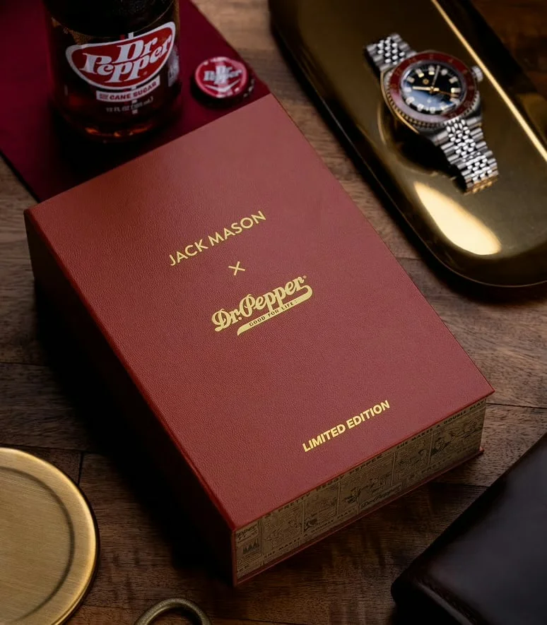 Jack Mason x Dr. Pepper limited edition box, Dr. Pepper bottle, watch on gold tray, coaster, and wallet on wood.