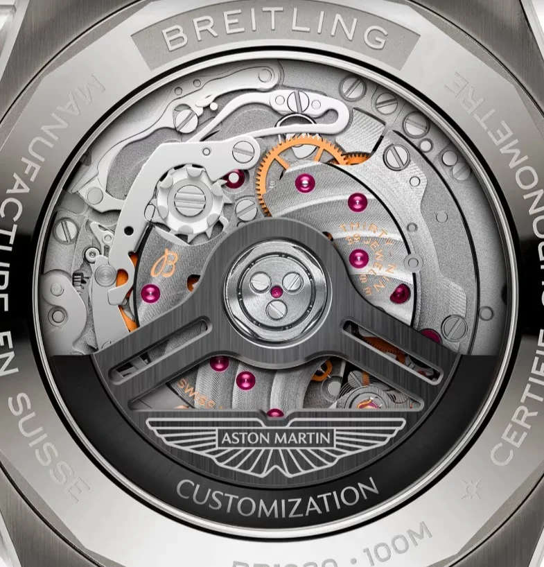 Breitling watch open case back showing intricate movement with gears, pink jewels, and Aston Martin branded rotor.