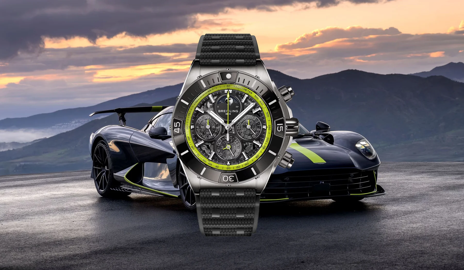 Breitling chronograph with green accents over dark sports car with green stripes. Mountain sunset.