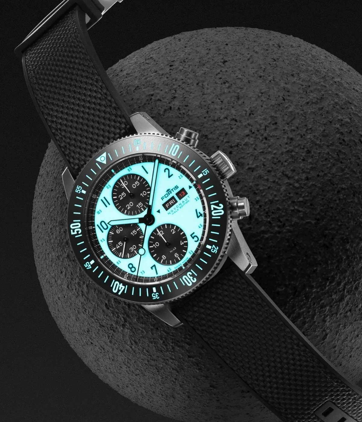 Fortis Novonaut Halo Edition chronograph with glowing light blue dial, black strap on a dark textured sphere.
