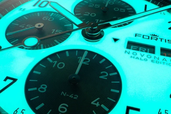 Macro shot of a glowing teal Fortis Novonaut Halo Edition chronograph watch face showing FRI 13.