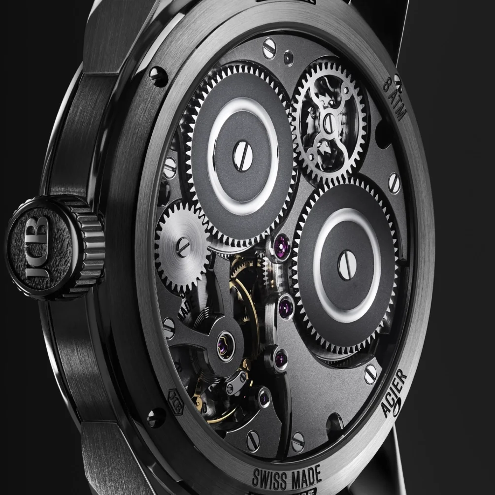 Close-up of a luxury watch's intricate movement, exposing gears, pink jewels, dark plates, and "JCB" crown.