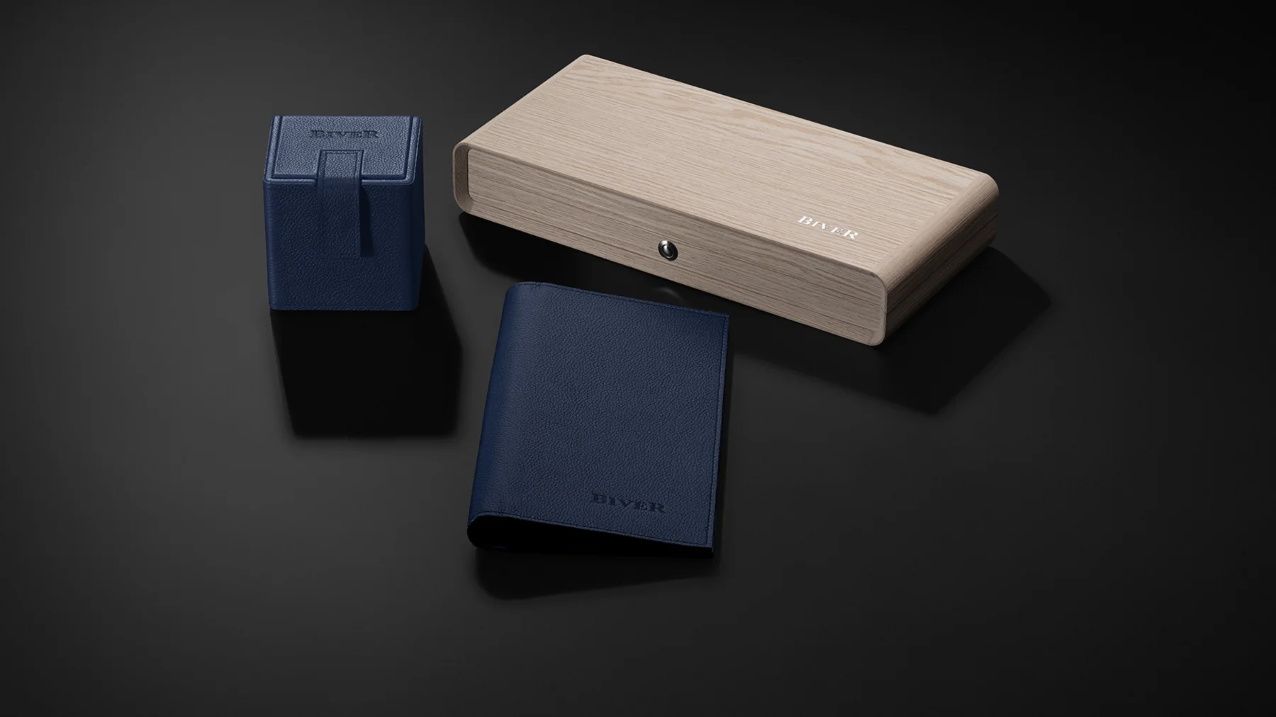 Three Biver branded items: navy leather watch case, matching booklet, and a light wood presentation box on a dark surface.