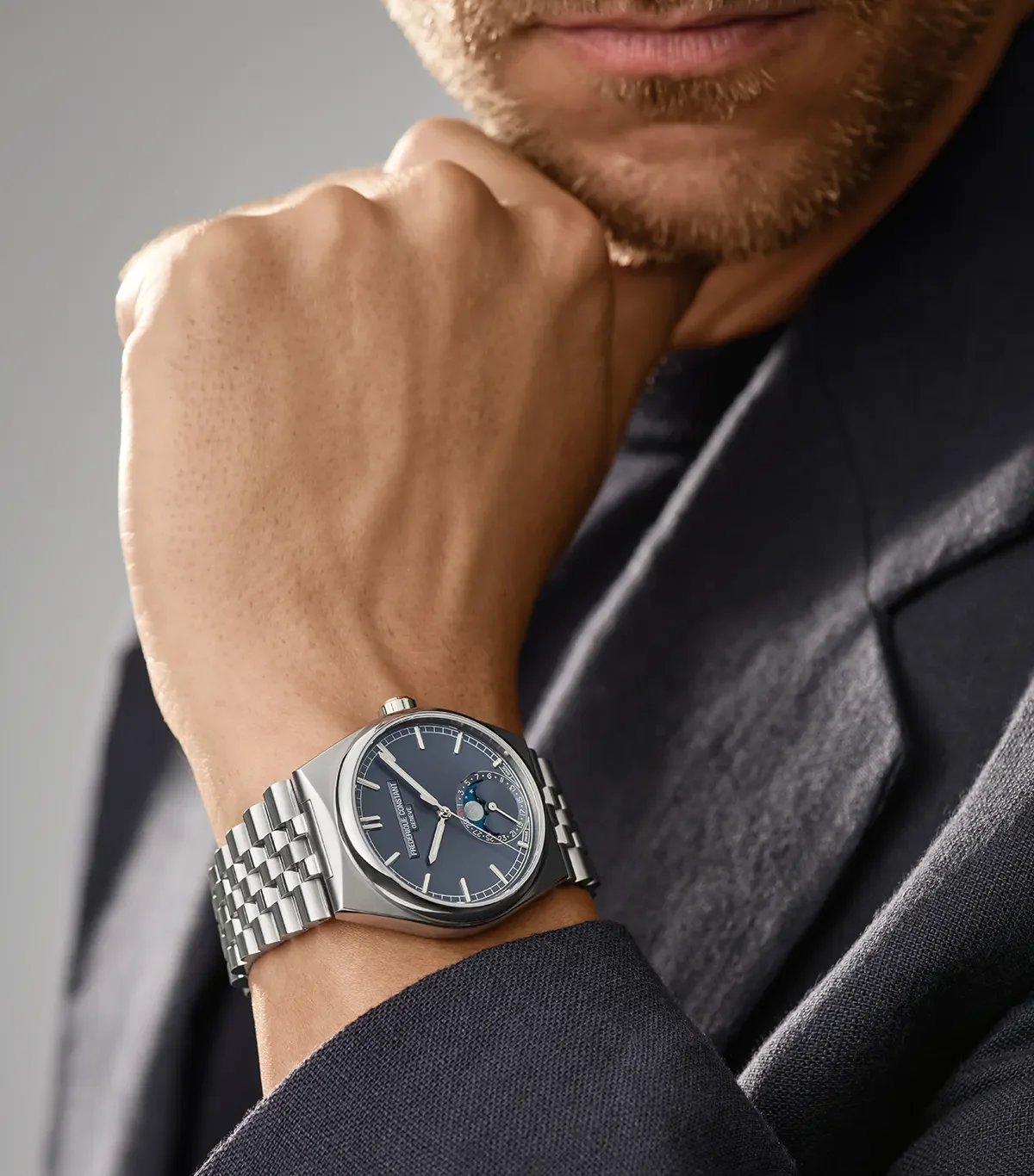 Man with beard & dark blazer wears a Frederique Constant blue moon phase watch on steel integrated bracelet.