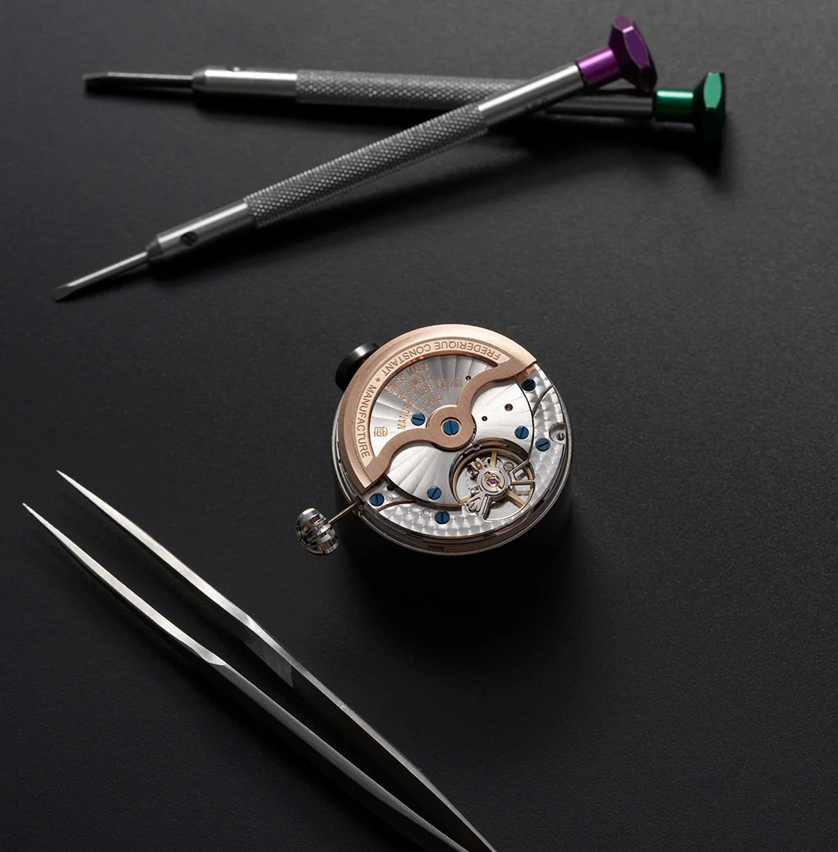 Frederique Constant watch movement, rose gold bridge, blue screws, with purple/green screwdrivers & tweezers.
