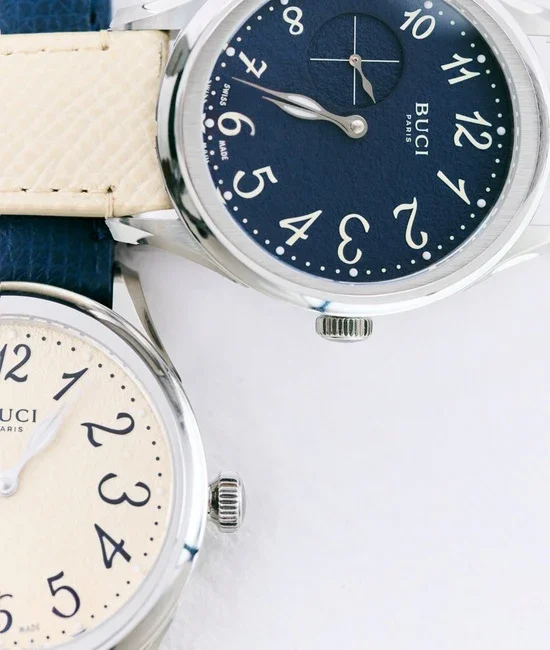 Close-up of two BUCI PARIS watches. Top: navy dial, silver case, cream strap. Bottom: cream dial, silver case.