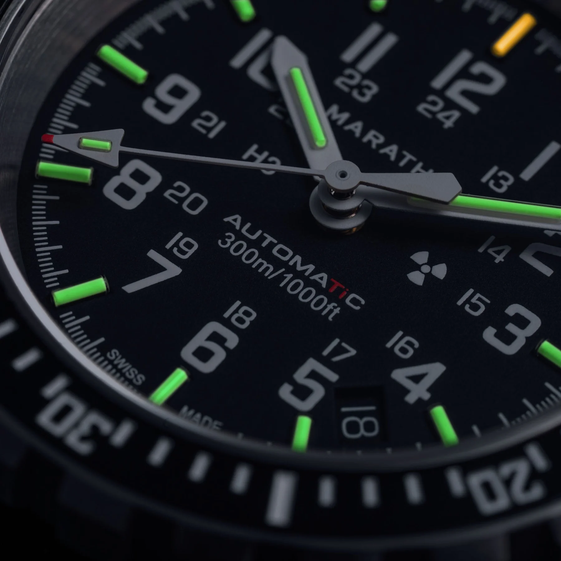 Close-up of a Marathon Automatic 300m dive watch, black dial, green luminous hands & markers, white 24hr numerals, radiation symbol, date 18.