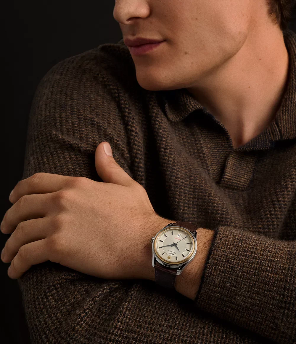 Man in brown knit wears a vintage-style Fossil watch with light dial, gold bezel, steel case, brown leather strap.