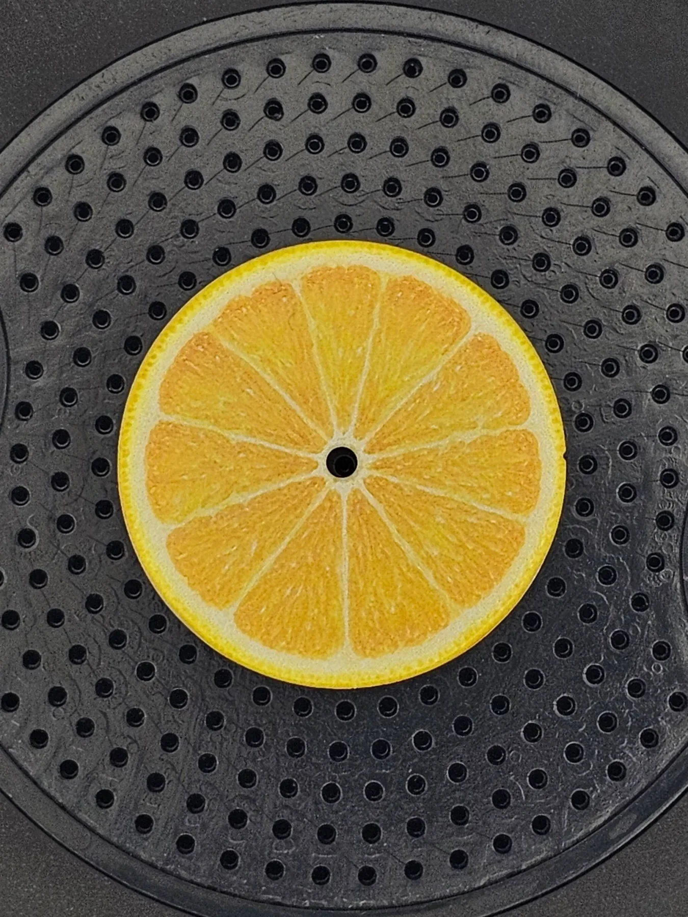 Stylized yellow lemon slice prop with central hole on dark, perforated circular surface.