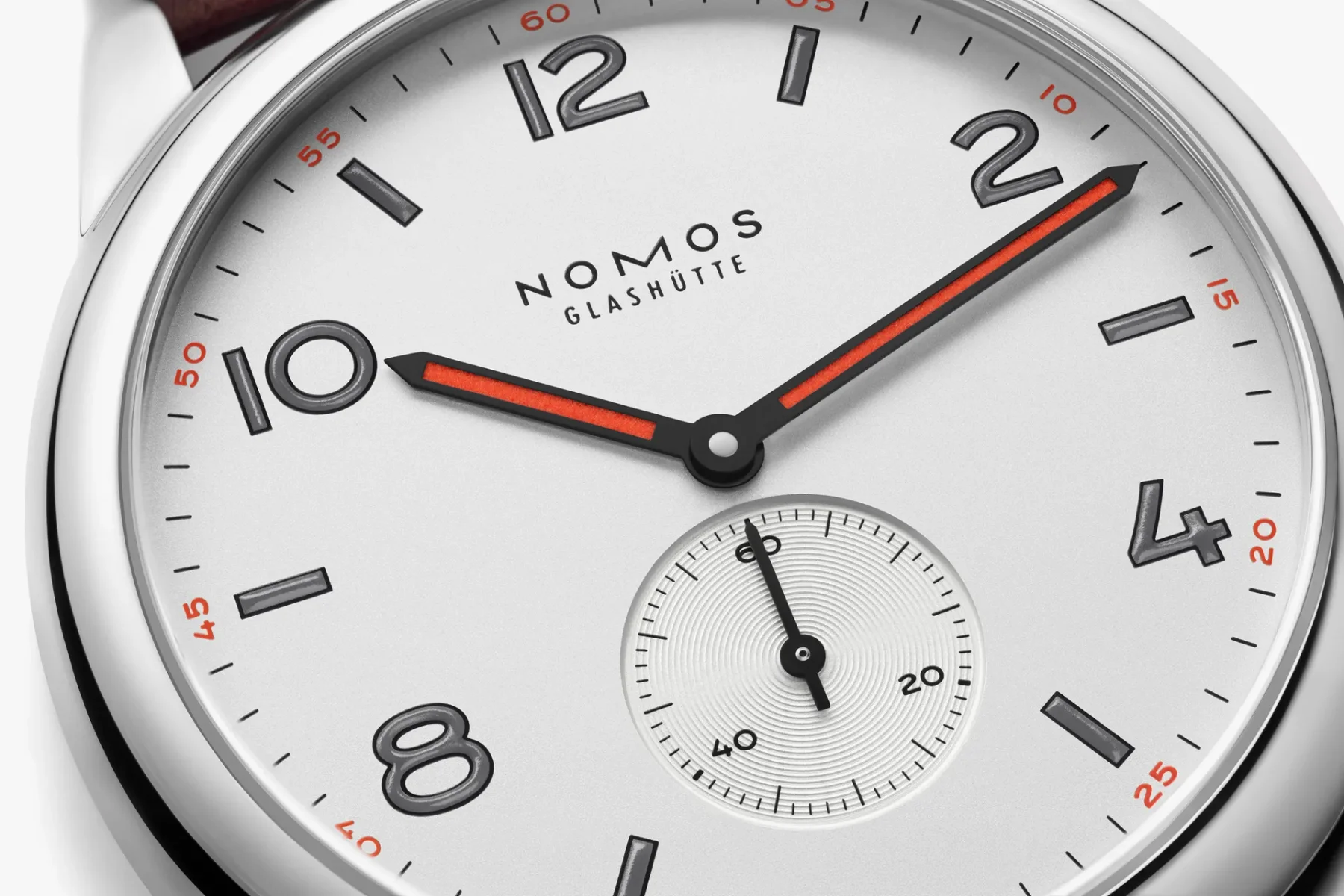 Nomos Glashütte watch dial close-up. White face, black numerals, red luminous hands, and small seconds sub-dial.