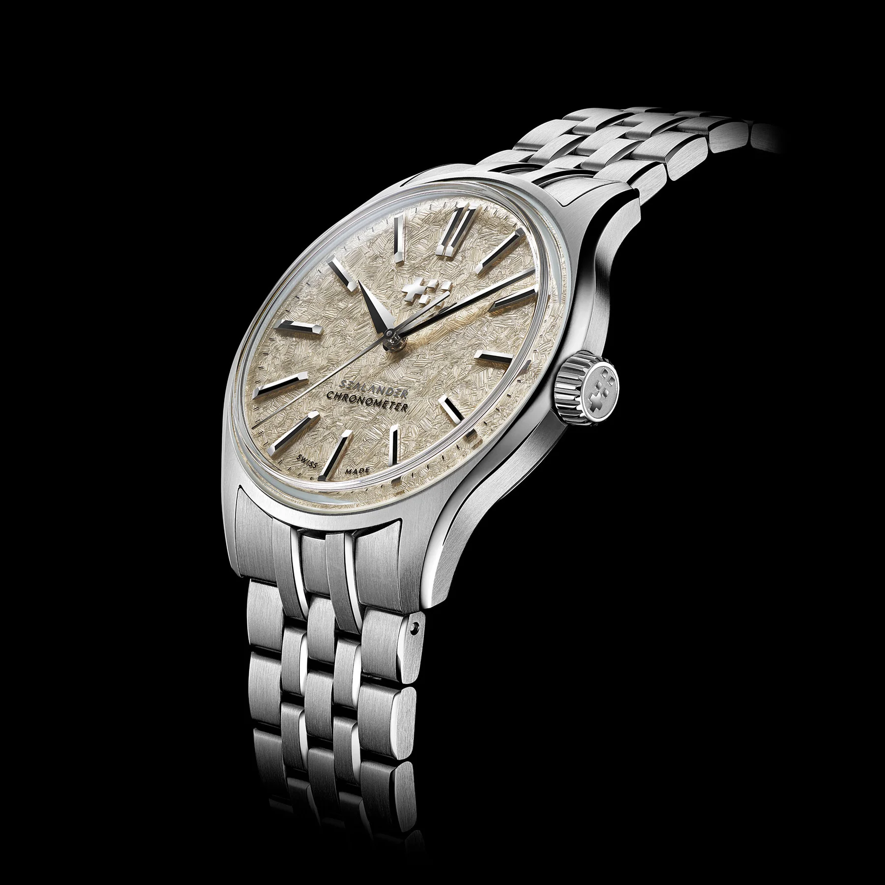 Stainless steel watch with a textured meteorite dial, applied markers, fluted crown, and steel bracelet, angled on black.