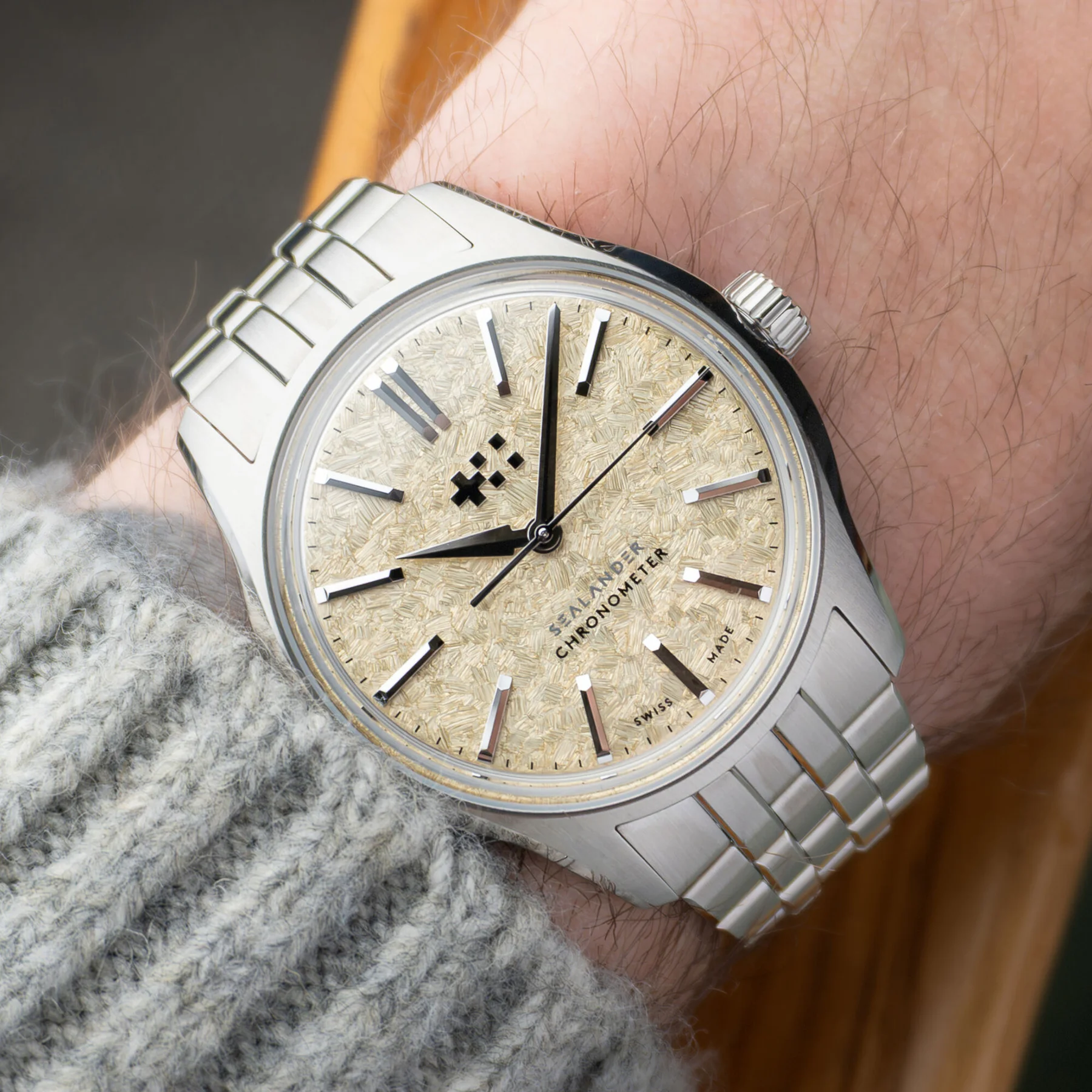Close-up: Sealander Chronometer watch with textured light gold dial, steel bracelet, on wrist with grey sweater.