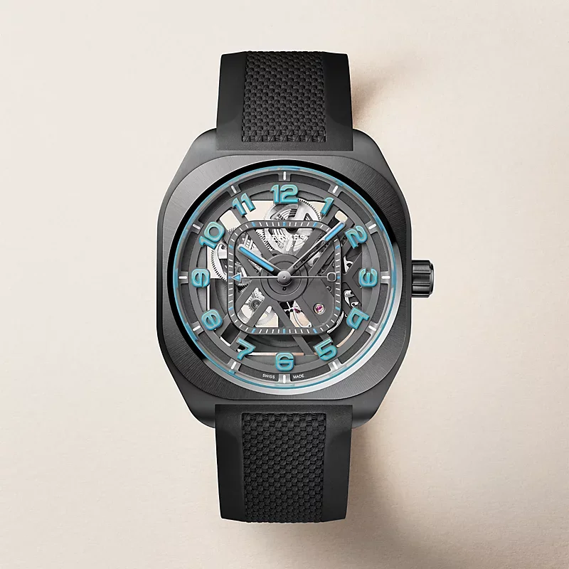 Dark grey luxury watch with skeletonized dial, light blue hands & numerals, and black textured rubber strap.