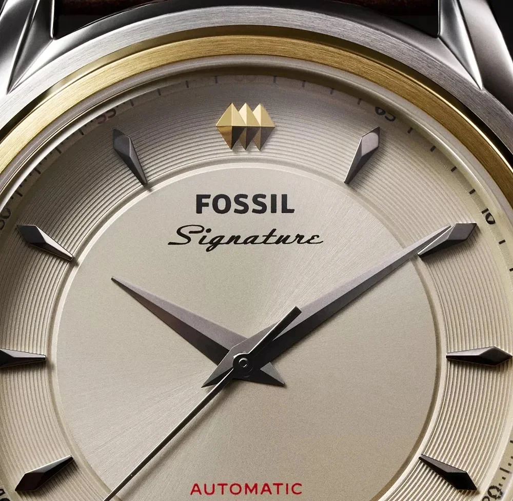 Close-up of Fossil Signature automatic watch. Textured silver dial, gold bezel, dark markers, gold emblem, brown strap.