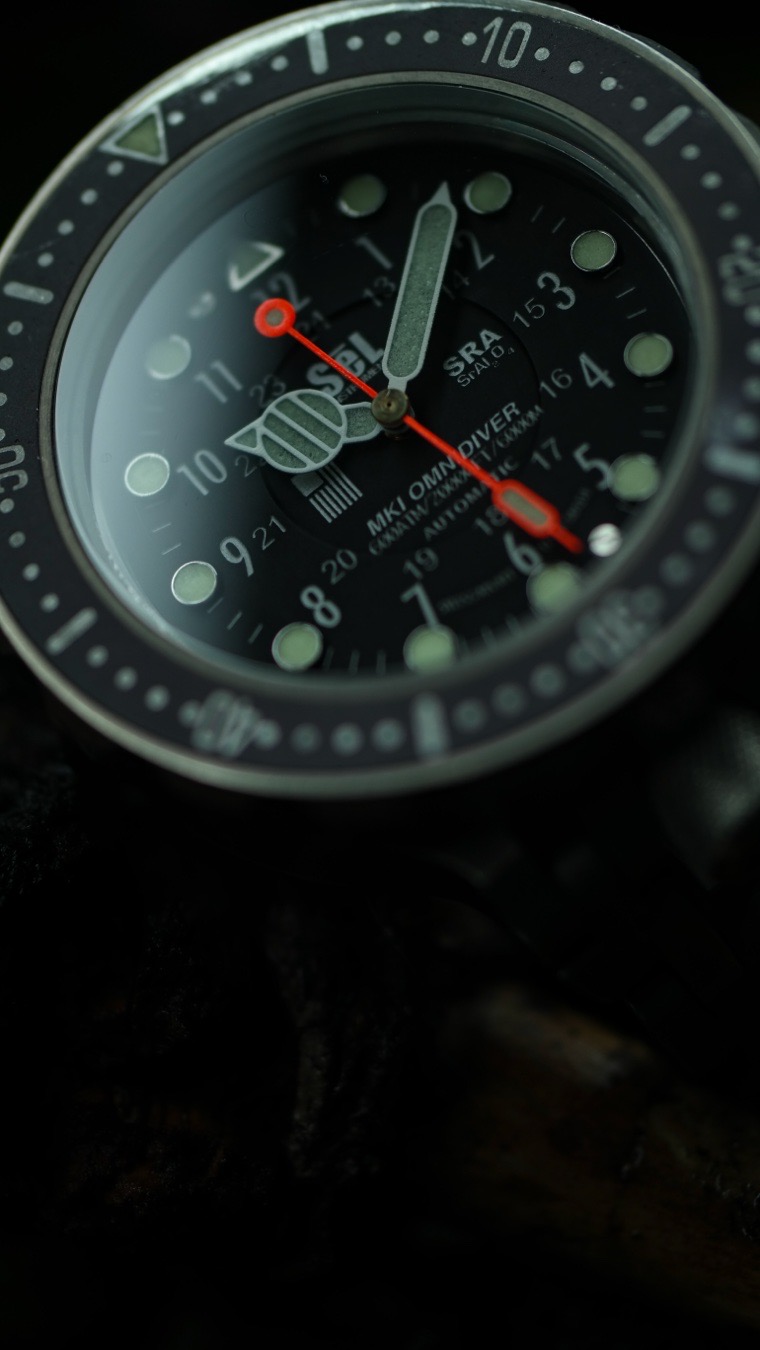 Hand-machined entirely in-house in Tucson, Arizona, from certified Grade 5 titanium, it is a 6,000-meter diver that revolutionized the concept of the hardcore tool watch. For enthusiasts wanting a wearable, bombproof wrist instrument, there is simply nothing else like it on the market.
The inception of SēL Instrument, driven by founder Andrew McLean, was fueled by a singular, unapologetic focus: true, uncompromised utility. While many historical luxury dive watches have slowly shifted toward fashion accessories, the OmniDiver MK1 is born from raw function first.
The dial layout is fiercely purposeful. Sizing is incredibly balanced for the wrist, and the dial features bright, lume-filled markers that guarantee elite legibility in all conditions. The crown is uniquely positioned at 6 o’clock and tucked perfectly between the lugs, shielding it from impacts while leaving it easily accessible.
What truly acts as the “killer app” of the OmniDiver series is the proprietary WavLock™ titanium bracelet. In an industry where most bracelets follow the exact same historical templates, SēL developed a fresh, industrial approach.
The WavLock clasp and bracelet assembly allow the wearer to adjust the band size on the fly—up to 24mm of incremental adjustment in 4mm steps—without the need for specialized tools. It also features an auxiliary 14mm dive extension so the watch can easily slip over a thick wetsuit. The bracelet articulates beautifully, conforming to the wrist while simultaneously looking like a rugged, heavy-duty piece of survival gear.
Because the OmniDiver MK1 uses certified Grade 5 titanium rather than cheaper, unverified alloys, the metal ages beautifully. It is the kind of watch that thrives on “battle damage.” Rather than worrying about a hairline scratch, collectors who live with the OmniDiver often embrace the darkened patina and the stories etched into the metal over years of harsh environments and daily adventures.