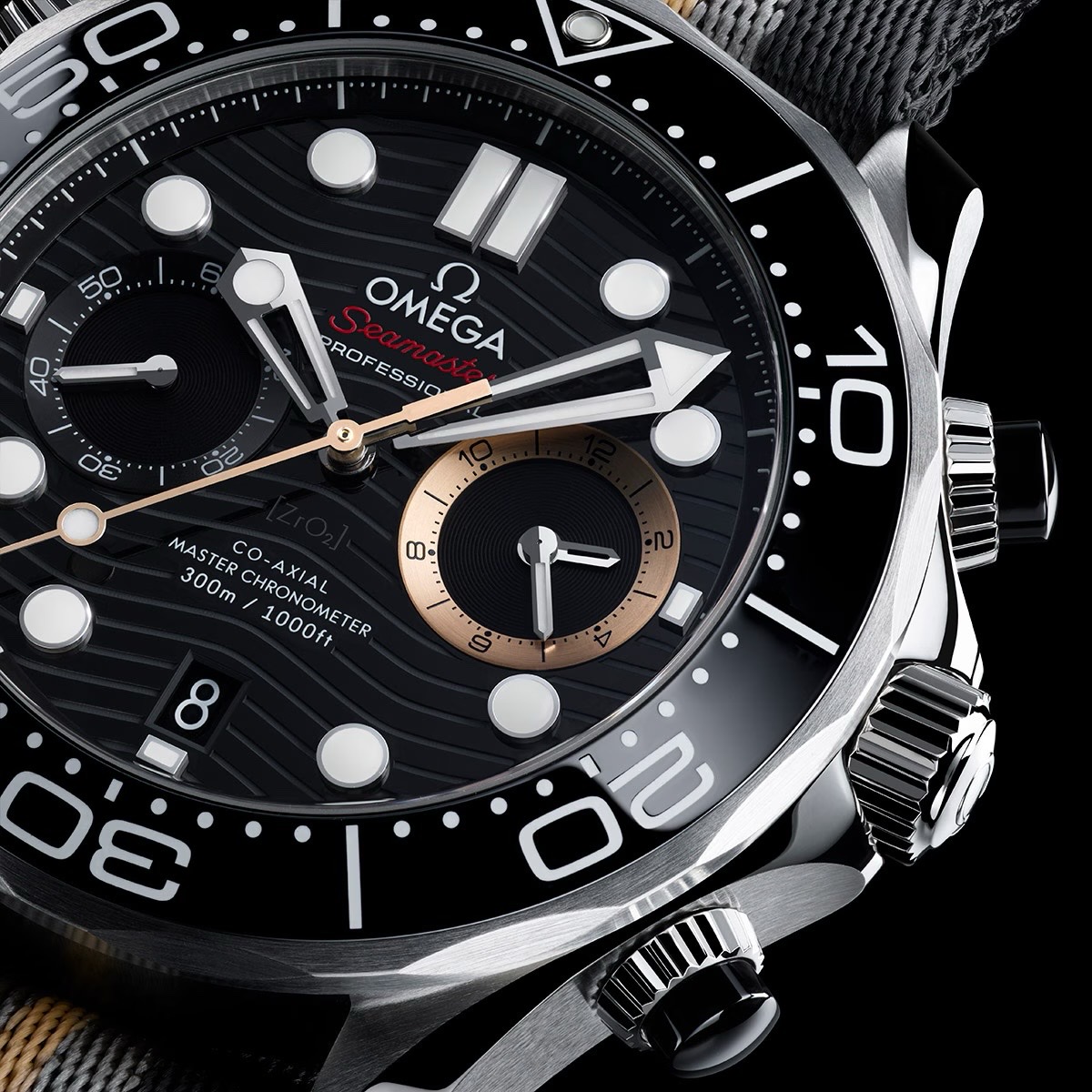 Close-up: black Omega Seamaster chronograph with wave dial, bronze accents, black ceramic bezel, and grey strap.