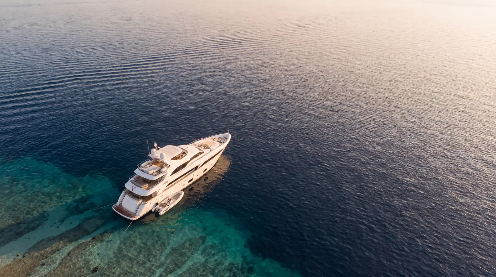 Aerial view of a motor yacht anchored over turquoise shallows