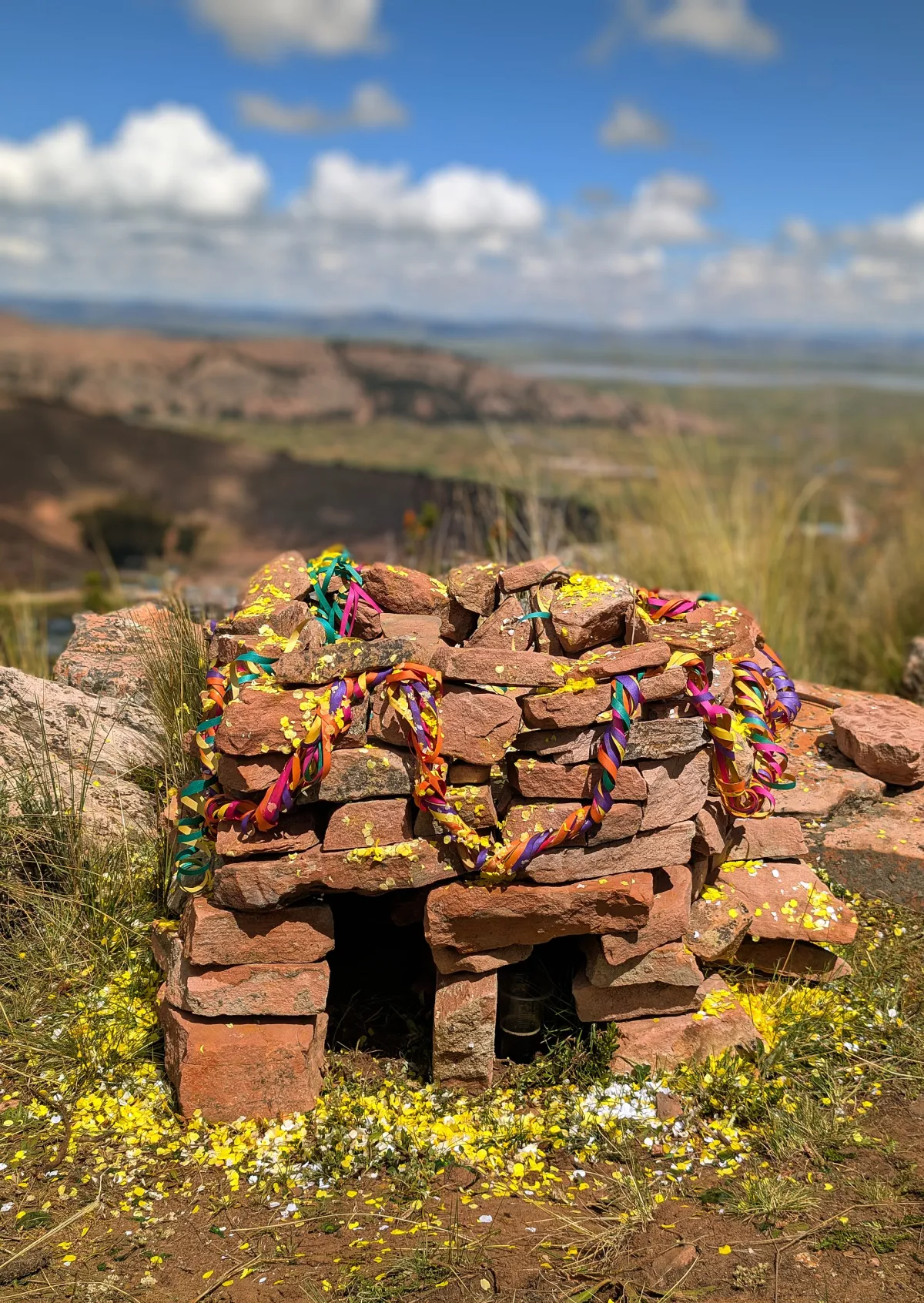 Un pequeño altar de piedra decorado con serpentinas y confeti en la cima de un cerro sobre un lago, tras un pago a la tierra