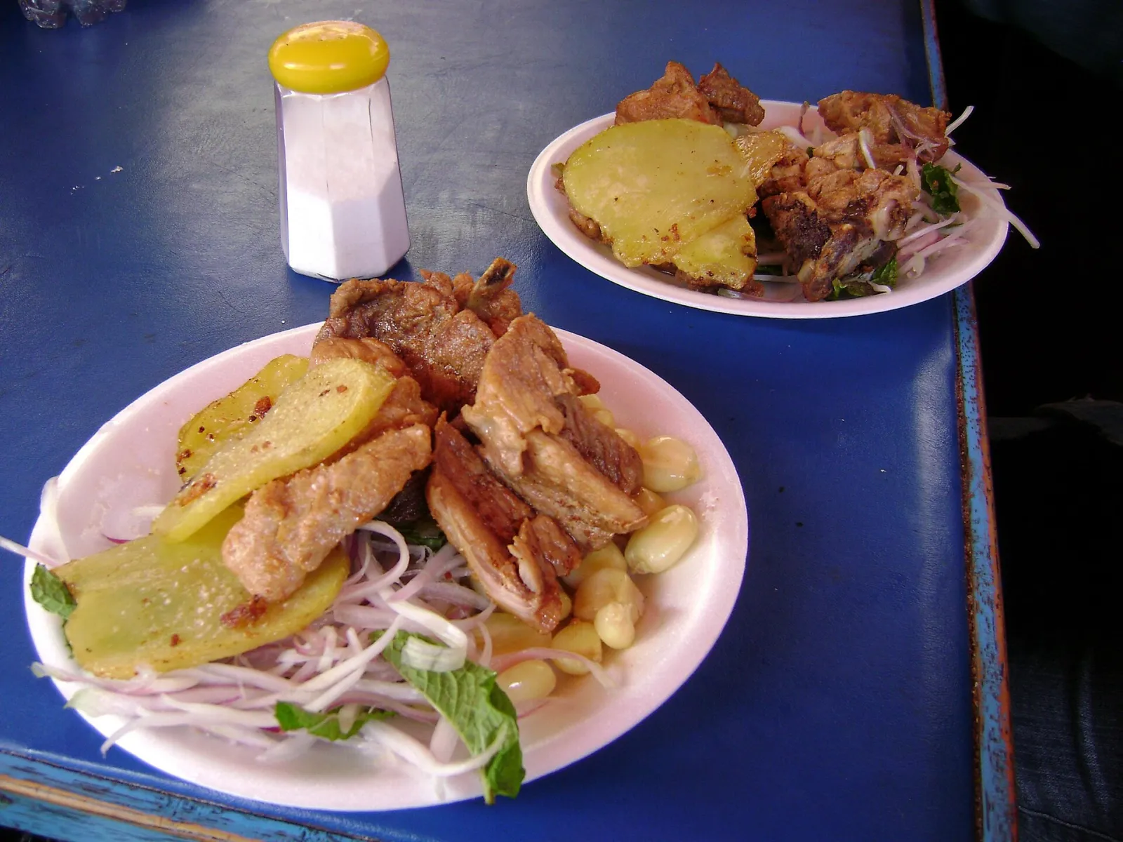 Two plates of Cusco chicharrón with fried potato, mote corn, red onion and mint