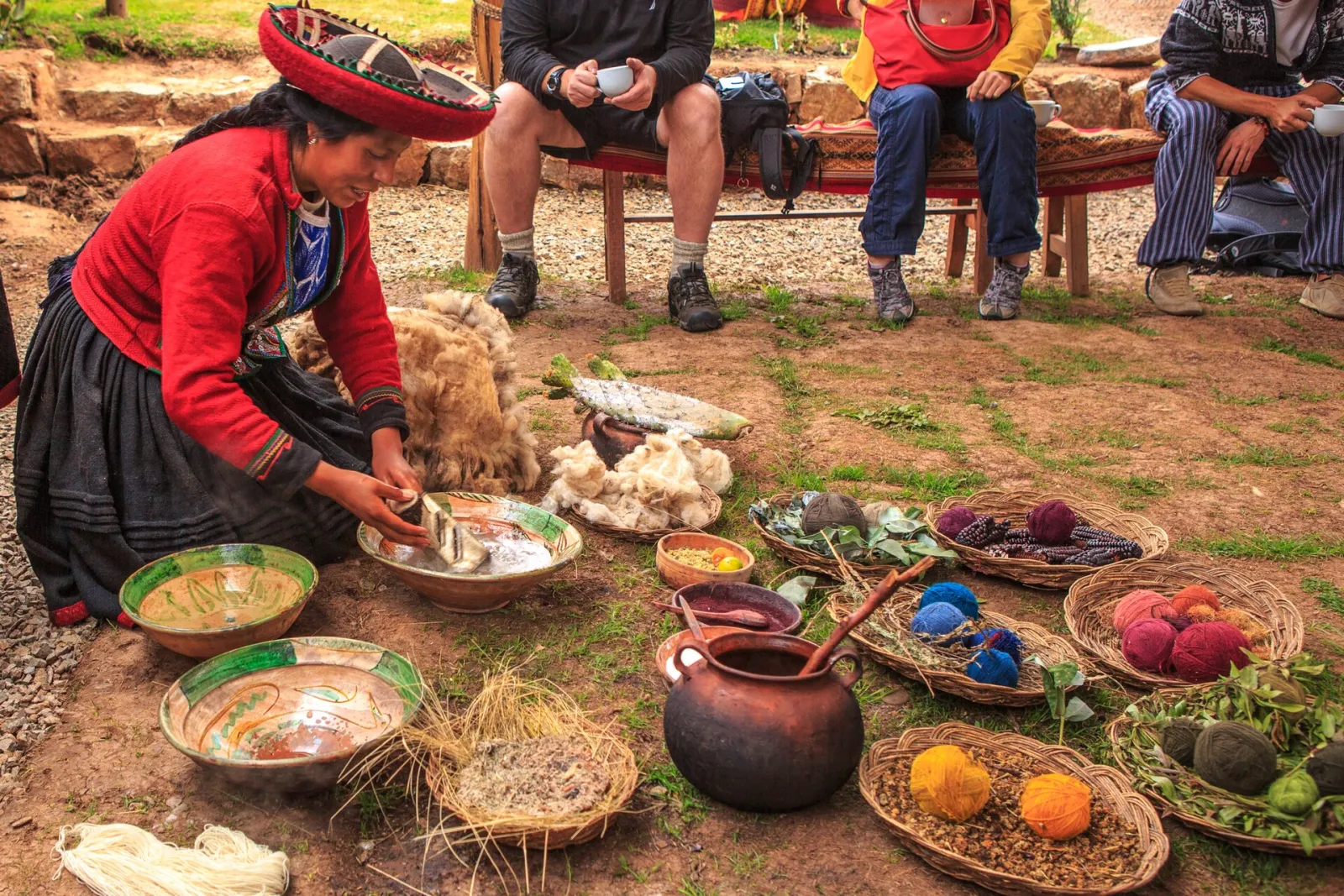 Una tejedora de Chinchero arrodillada entre cuencos con plantas y lana teñida, mostrando a visitantes cómo se tiñe con tintes naturales