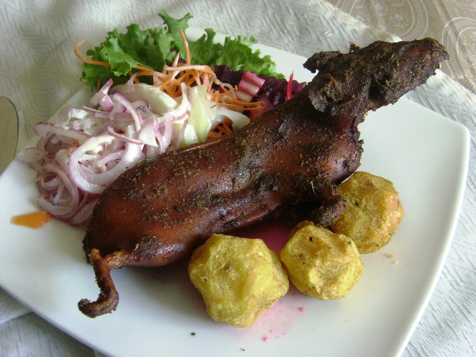Roasted cuy served with golden potatoes and a fresh salad