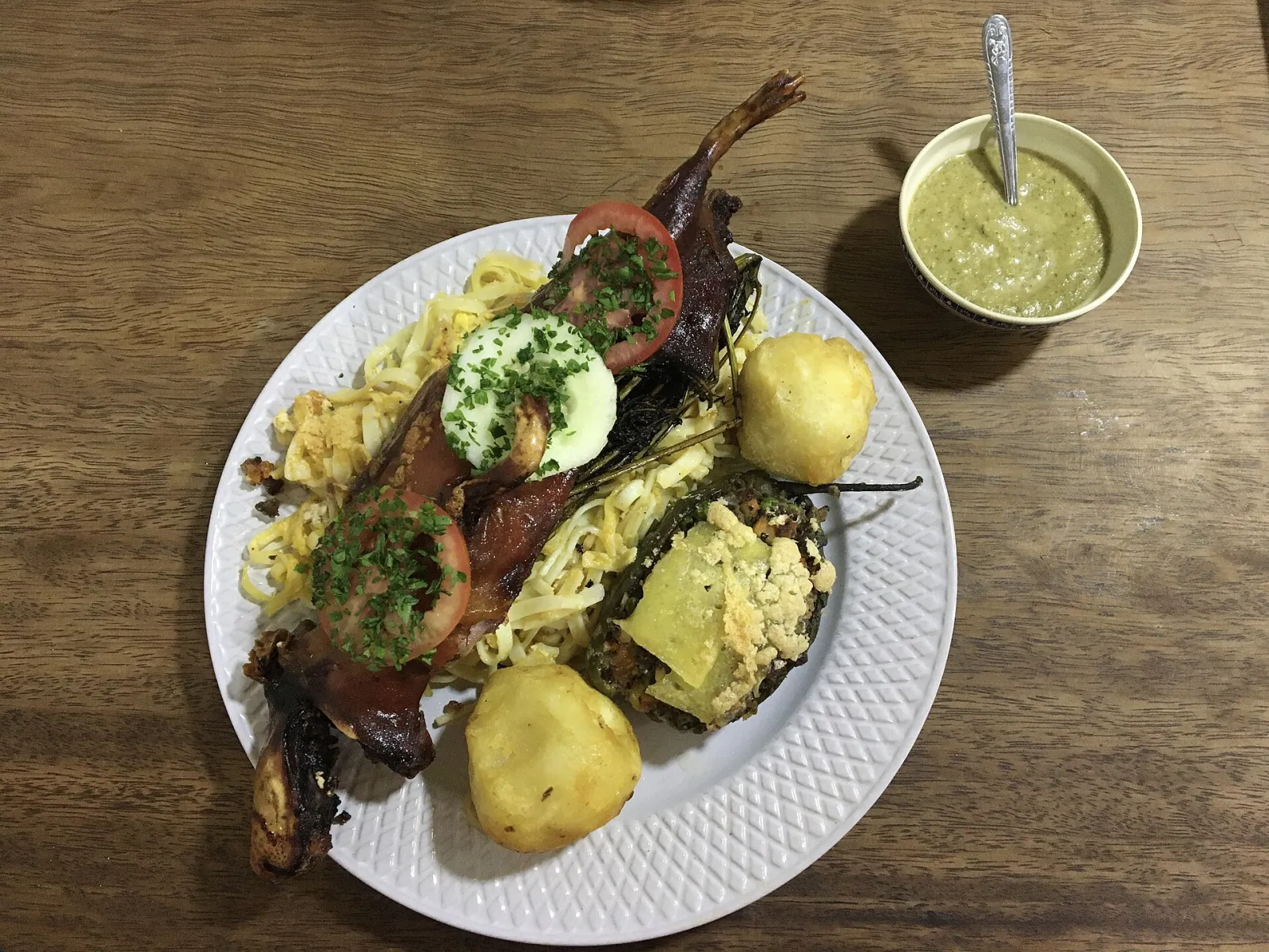 Cuy al horno on a white plate with noodles, potatoes, a stuffed rocoto and a bowl of green sauce at La Chomba in Cusco