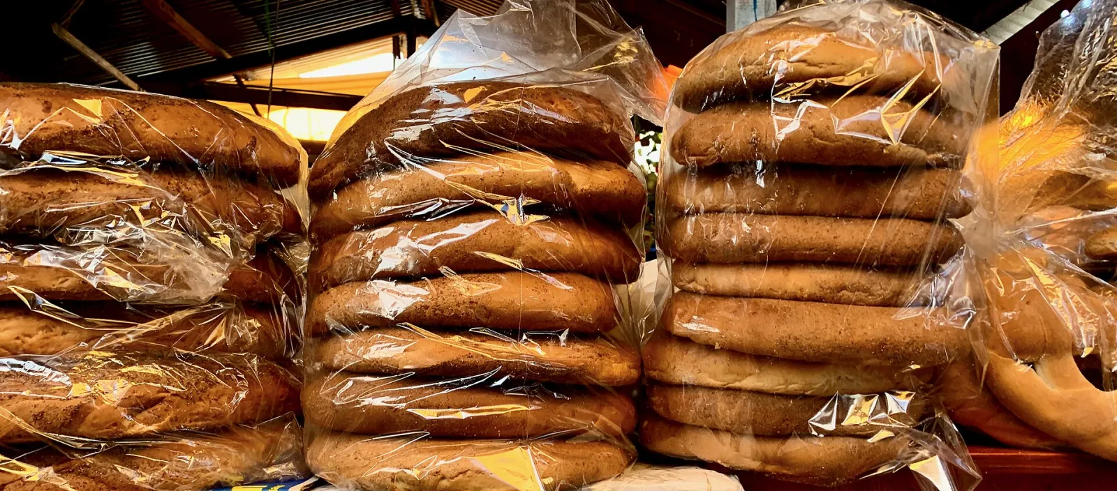 Stacks of large round pan chuta loaves wrapped in plastic at a market stall