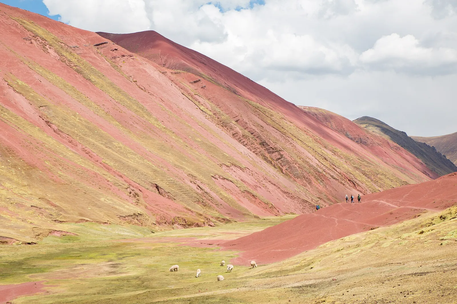 Hikers walking down the rust-red slopes of the Red Valley after visiting Rainbow Mountain