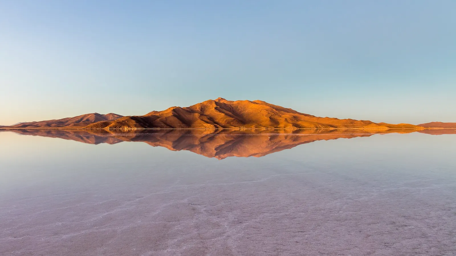 O salar de Uyuni refletindo um morro avermelhado com luz baixa