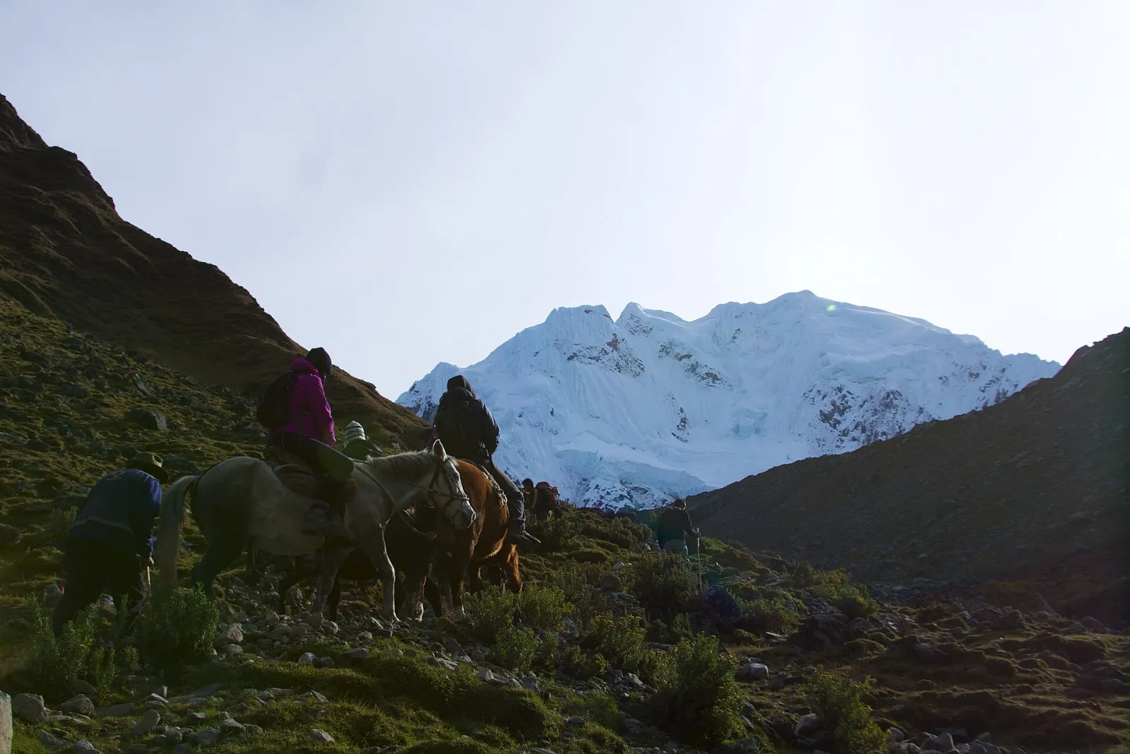Riders on horses climbing toward the Salkantay Pass below a snow peak