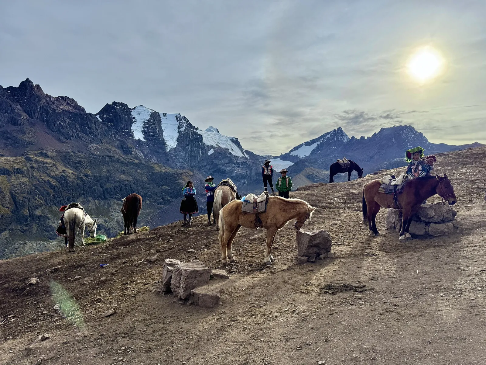 Saddled horses and their handlers waiting on the upper trail to Vinicunca, with snow peaks behind