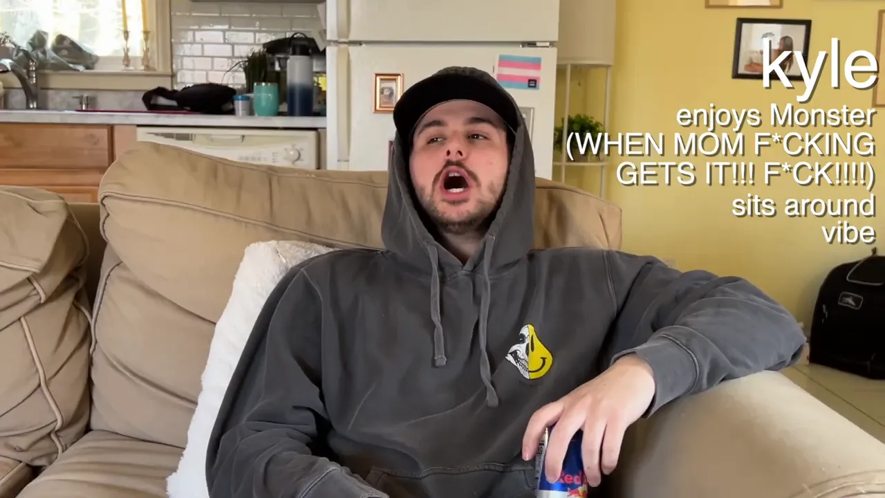 person in a hoodie and cap sitting on a couch opening a can with text on screen that says enjoys monster