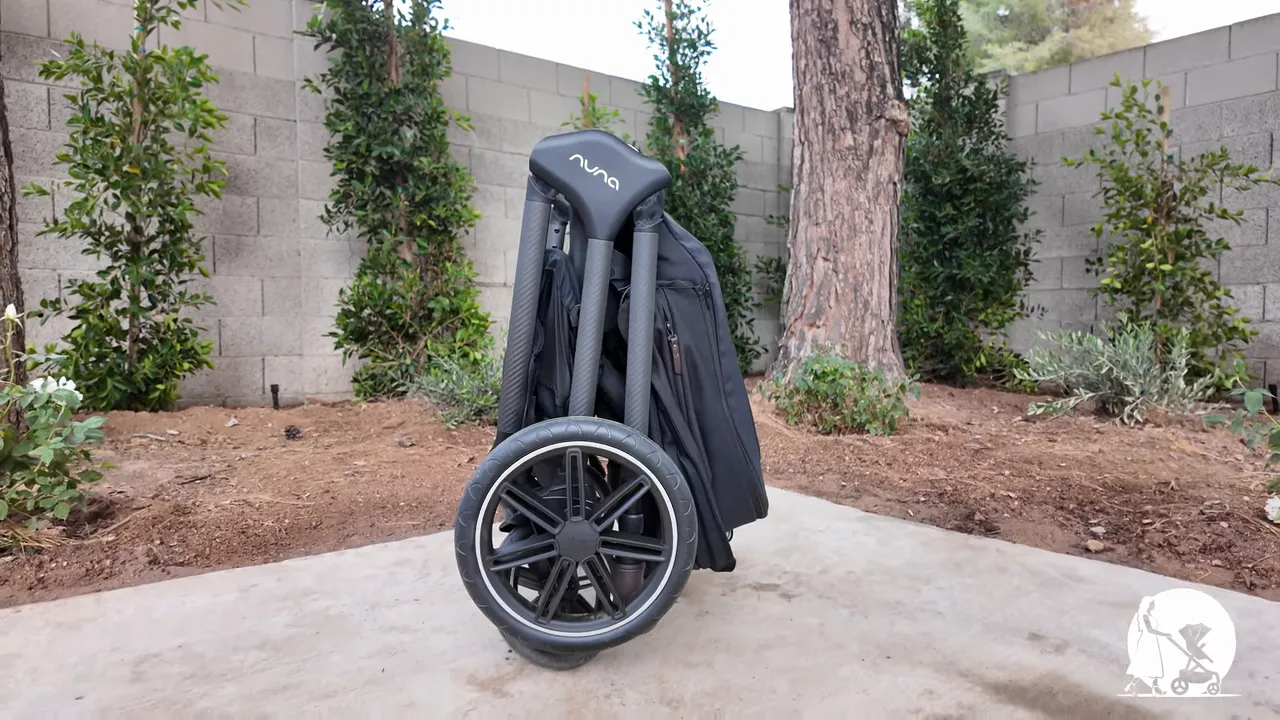 Reviewer lifting the folded Nuna TRIV LX stroller by its carry strap demonstrating standing fold and portability