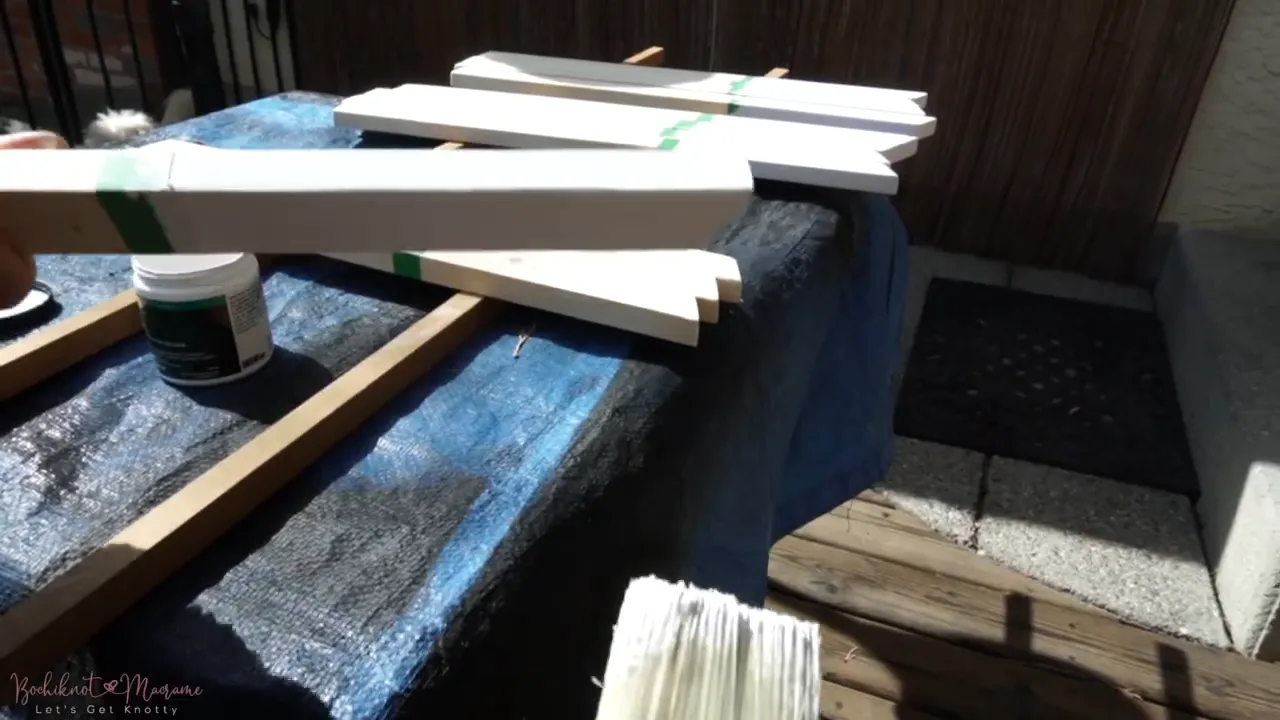 paintbrush applying white paint to a masked wooden leg end, jar of paint visible at the edge