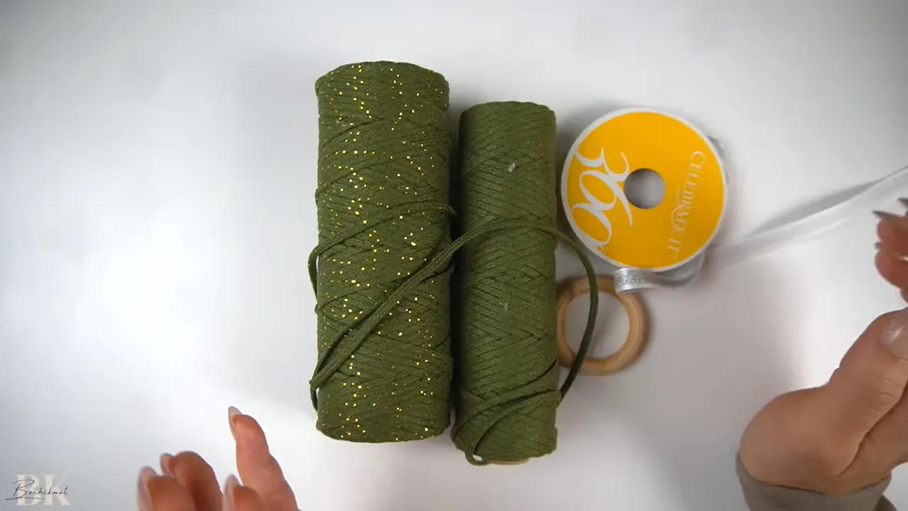 Slightly blurred view of two spools of green cord, ribbon and hands holding a short cord piece