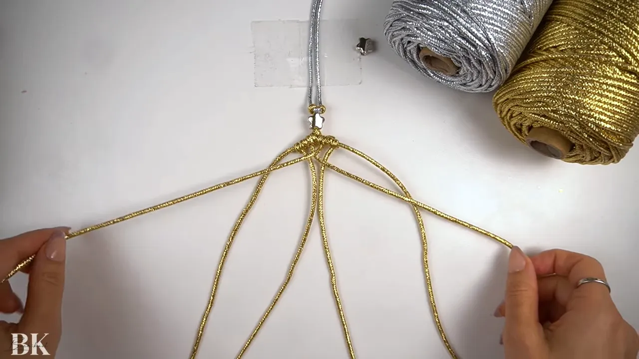 hands arranging gold macrame cords under a taped handle with silver and gold cord spools visible