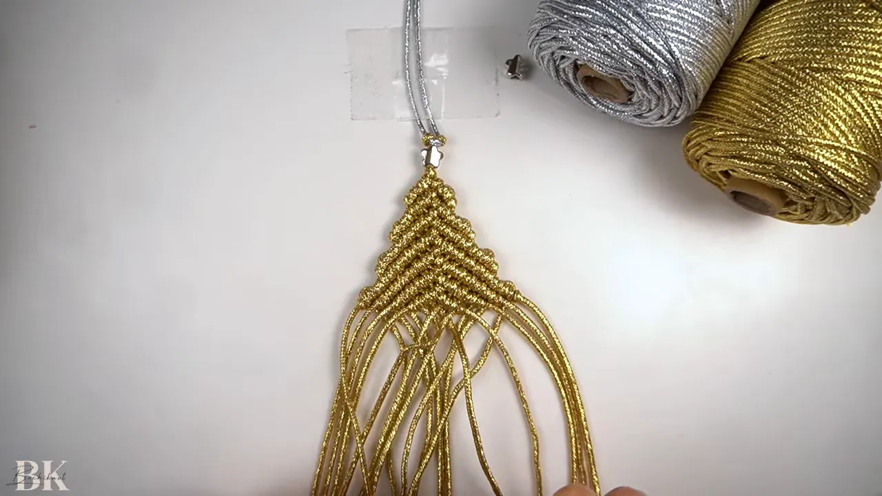 Close-up of hands filling the middle rows of a gold macrame Christmas tree ornament, forming a clear triangular taper.
