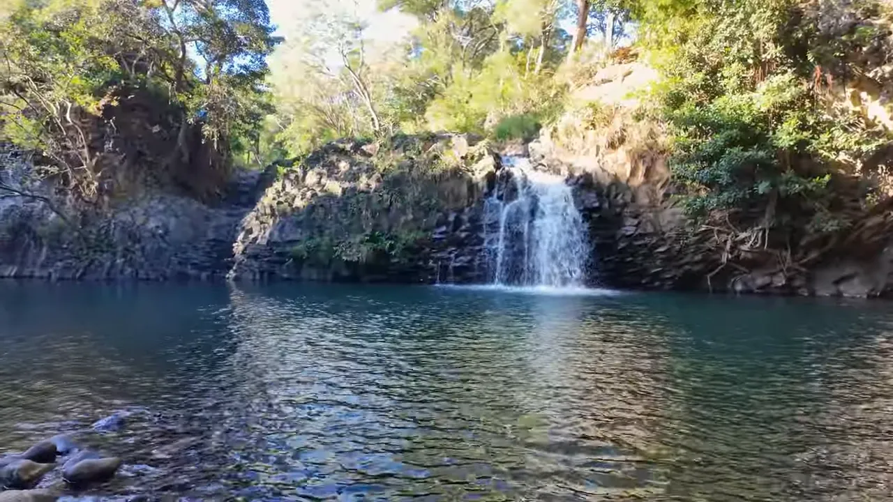 Overhead view of upper cascades feeding into a rock-lined pool with dense foliage on the banks.