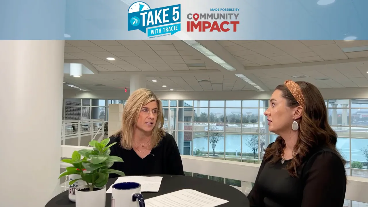 Tracie and Jennifer seated at a table mid-conversation with a potted plant and coffee mugs, bright studio environment.