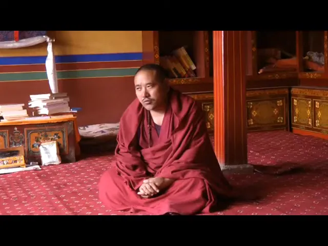 Monaco tibetano seduto su un tappeto tibetano rosso con motivi geometrici all'interno di un tempio