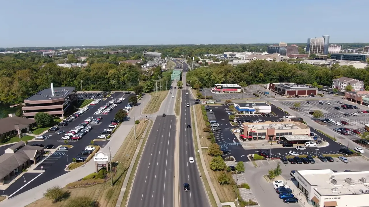 Aerial view of a suburban neighborhood with a pond and fountain, houses, driveways and green lawns.