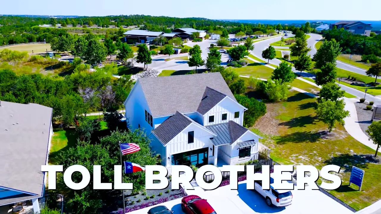 Presenter gesturing toward the front of a white Ladybird farmhouse-style model home at Headwaters with driveway and parked cars