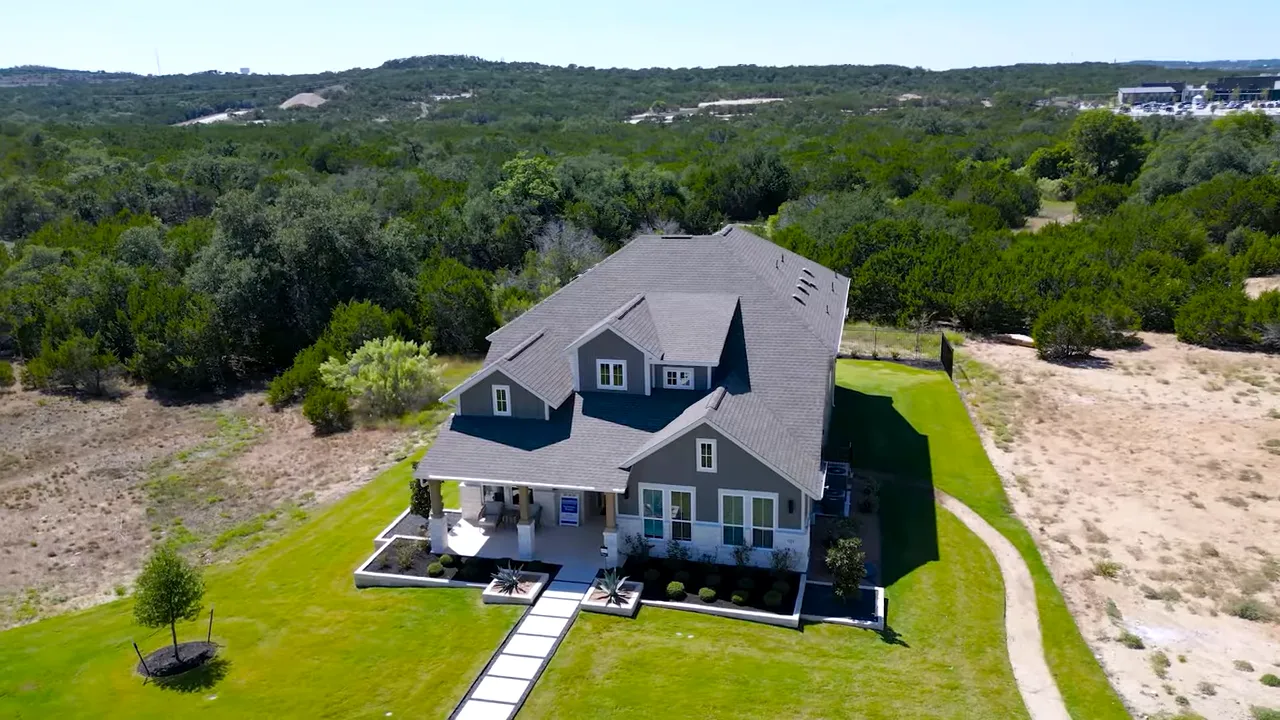 Aerial view of a fenced backyard and adjacent natural lot at Headwaters with hill country in the distance