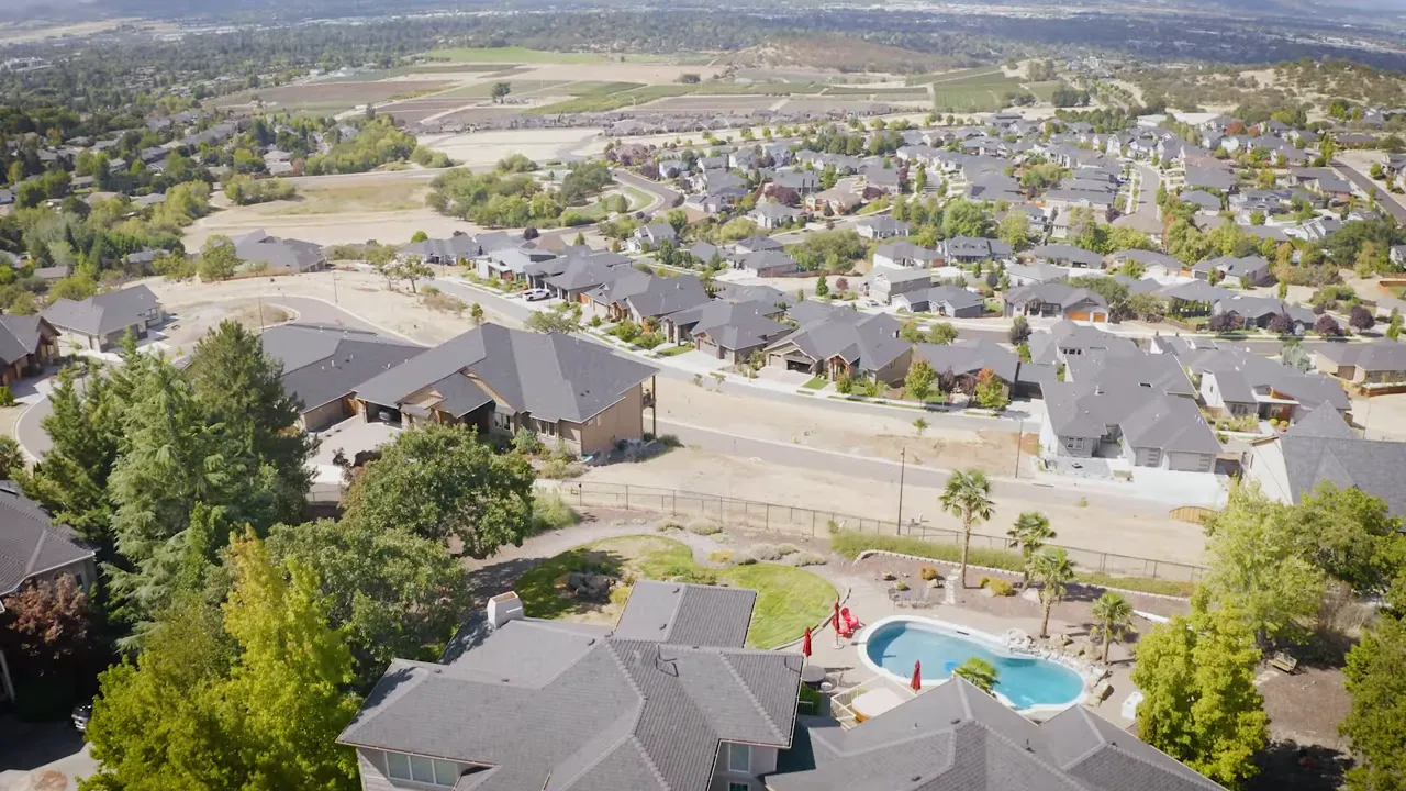 Two men talking during an on-the-street interview in an outdoor downtown plaza with storefronts and seating in the background.