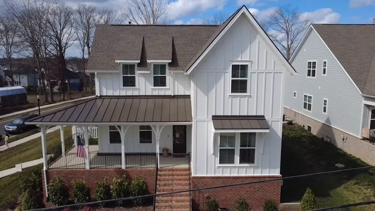 Aerial view of white home with wraparound porch and fenced yard
