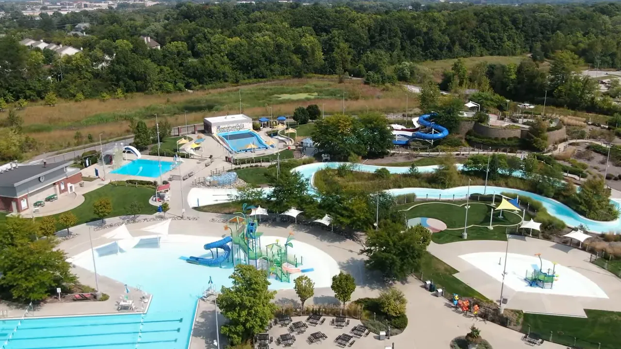 Aerial view of downtown Indianapolis with stadiums, office buildings and an urban park under a clear blue sky with 'Living in Indianapolis' overlay.