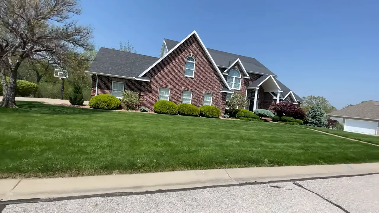stone house with steep roofline, curved driveway, and striped green lawn